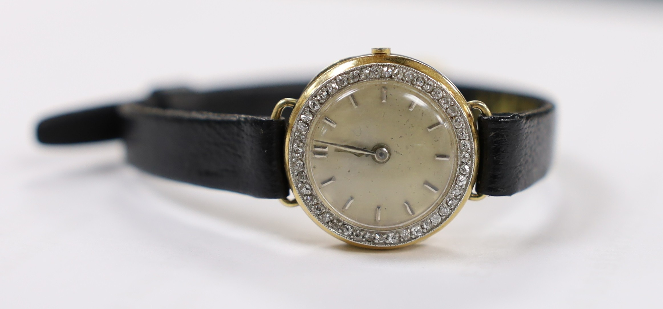A lady's 18k manual wind wrist watch, with diamond set bezel and dial with baton numerals (a.f.), on a leather strap, lacks winding crown.